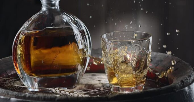 An ice cube slowly falls into a glass of whiskey on top of a vintage whiskey barrel. A decanter with a drink stands nearby, a dark brown background. Blackmagic Ursa Pro G2. 