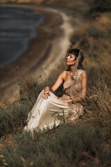 A beautiful girl in a stylized suit sits on a mountain above the sea, lake on a sunny day.