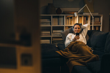 young woman listening to a music on headset. she is relaxing on sofa at her living room. evening...