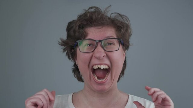 Emotional crazy young woman laughs smile without tooth, ruffles her hair and wrinkles into camera in studio. Funny toothless female has gone crazy. Mental health, anxiety, stressed out concept