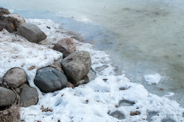 Melt water along the rocky shore of the pond. Remains of ice on the surface of the pond.