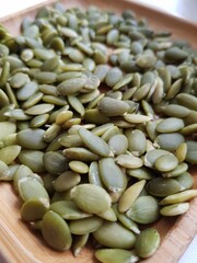 Green pumpkin seeds lie on a wooden plate