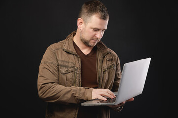 A portrait of a focused Caucasian man with a laptop in his hands stands in the studio and looks attentively into the laptop. The concept of using pc and mobile remote access to services