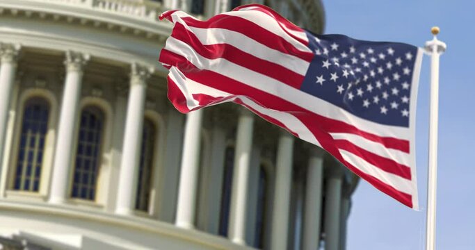 The flag of the united states of america flying in front of the capitol building blurred in the background