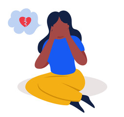 A young african american girl sits on the floor and cries, the girl covered her face with her hands. A frustrated girl with a broken heart