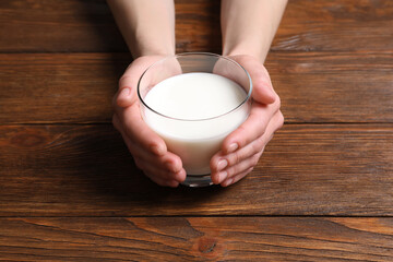 Woman holding glass of milk at wooden table, closeup
