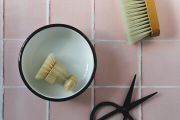 Black and white flat lay composition of utensil on a pink tile kitchen or bathroom floor background, top view. Eco-friendly stylish cleaning brushes and tools.