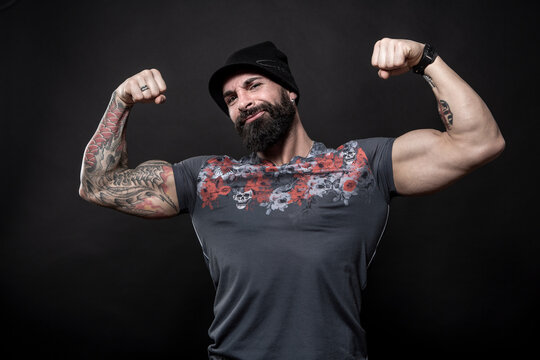 Uomo moro muscoloso con maglietta color fantasia e cappellino in lana, mostra i muscoli orgoglioso , isolato su sfondo nero

