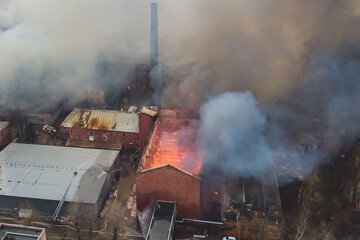 Massive large blaze fire in the city, aerial drone top view brick factory building on fire, hell...