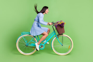 Photo of sweet hurrying young woman dressed blue outfit driving bike looking empty space isolated green color background