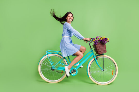 Photo of pretty funny young lady wear dotted clothes smiling driving bicycle isolated green color background