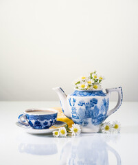 Blue and white teapot, lemon and daisies on white. Copy space