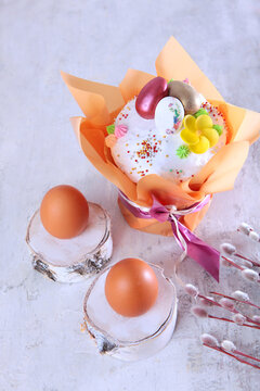 Easter cake in a festive package on a light background. Willow branches.The concept of the Easter holiday. Free space. Chicken eggs on wooden stands. Vertical photo.