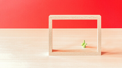 An empty wooden photo frame and a scaled-down green mock-up of a man's hand