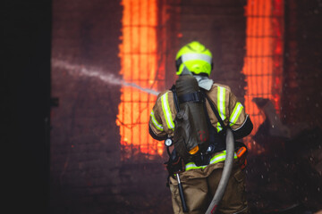Naklejka premium Firefighters put out large massive fire blaze, group of fire men in uniform during fire fighting operation in the city streets, firefighters with the fire engine truck fighting vehicle