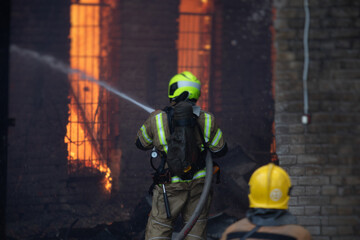 Fototapeta premium Firefighters put out large massive fire blaze, group of fire men in uniform during fire fighting operation in the city streets, firefighters with the fire engine truck fighting vehicle