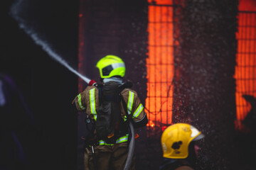 Firefighters put out large massive fire blaze, group of fire men in uniform during fire fighting operation in the city streets, firefighters with the fire engine truck fighting vehicle