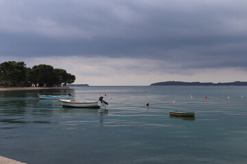 Fototapeta na wymiar Thunderous sky and calm sea with boats, gray clouds are reflected in calm blue water. Seascape calm at sea, boats anchored storm clouds, island Brijuni on the horizon, Croatia