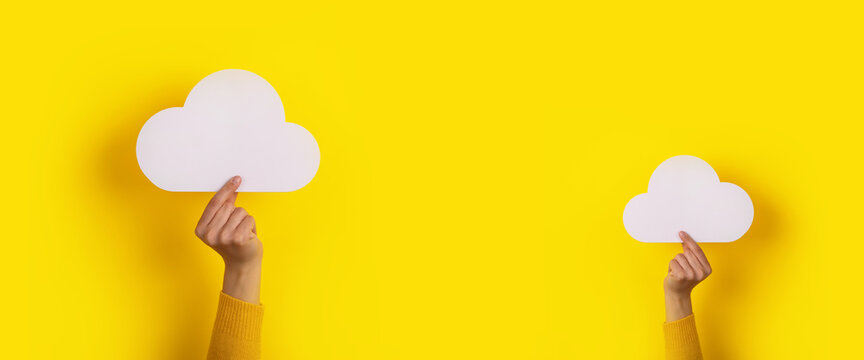 Two hands holding paper cloud over yellow background, panoramic image, cloud storage concept