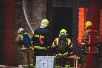 Fototapeta premium Firefighters put out large massive fire blaze, group of fire men in uniform during fire fighting operation in the city streets, firefighters with the fire engine truck fighting vehicle