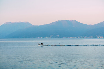 White motor boat tows small rowboats on the sea along the mountains at sunset