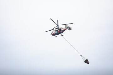 Fire fighting helicopter silhouette with bambi bucket for сarrying water to put out a massive building city fire, process of put out a large blaze bush fire wildifre, aerial firefighting with chopper