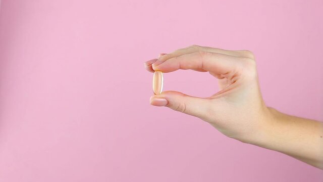 Omega 3 capsule in a female hand on a bright colored background close-up. 
