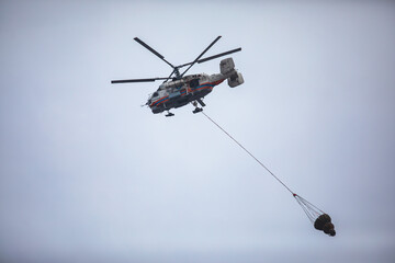 Fire fighting helicopter silhouette with bambi bucket for сarrying water to put out a massive building city fire, process of put out a large blaze bush fire wildifre, aerial firefighting with chopper