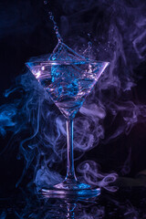 Splashing drink and purple-blue swirls of smoke on black background. On trend iced cocktail for advertisement of night club and party.