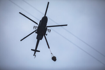 Fire fighting helicopter silhouette with bambi bucket for сarrying water to put out a massive building city fire, process of put out a large blaze bush fire wildifre, aerial firefighting with chopper