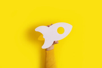 hand holding rocket over trendy yellow background, startup idea