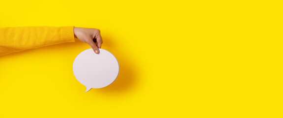 Talk bubble speech icon in hand over yellow background, panoramic layout