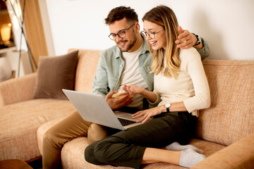 Young couple using laptop together while sitting on sofa at home