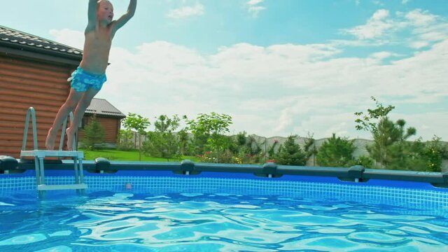 Slow motion clip: Happy boy having fun in the private pool.  White boy jumps into the pool creating a big splash. Child dives into the water in  summer. Activity of the child in the water. Happiness