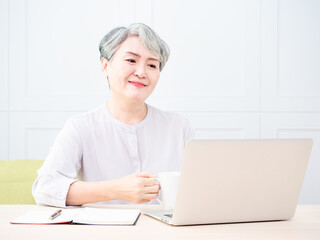 Senior asian woman using wireless laptop apps browsing internet and drinking coffee.