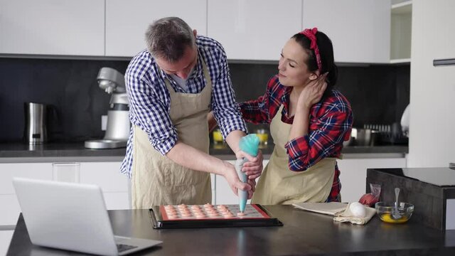 Man piping out macaron mixture on a slip mat with wife's support