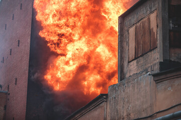 Massive large blaze fire in the city, brick factory building on fire, hell major fire explosion flame blast,  with firefighters team firemen on duty, arson, burning house damage destruction