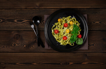 Green pasta with spinach, cherry tomatoes and cheese, on a wooden table, horizontal, no people,
