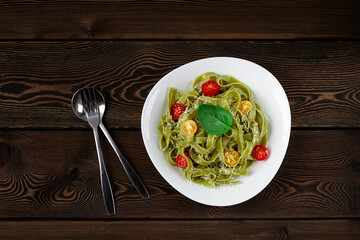 Green pasta with spinach, cherry tomatoes and cheese, on a wooden table, horizontal, no people,