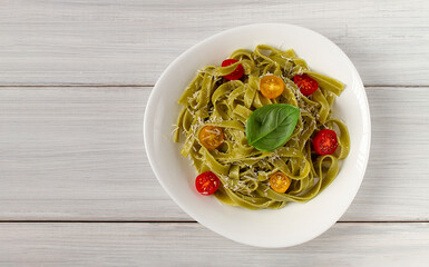 Green pasta with spinach, cherry tomatoes and cheese, on a white table, horizontal, no people,