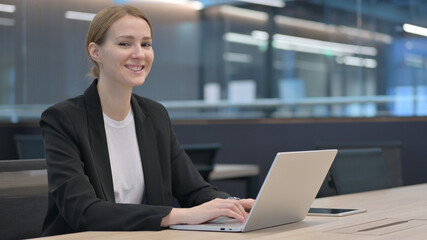 Businesswoman Looking at Camera while working on Laptop 