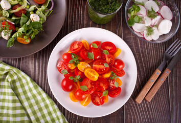 salads of fresh cherry tomatoes, mozzarella, basil and other greens on the dinner table