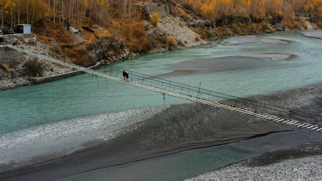 Two Local Women Carefully Crossing Hussaini Suspension Bridge Over Hunza River In Pakistan. - aerial orbit