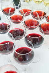 A large number of glass goblets filled with red wine are neatly arranged on the banquet table for the celebration. Wine is a type of alcoholic beverage.