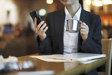 Businesswoman reading news on smartphone and drinking coffee in cafe