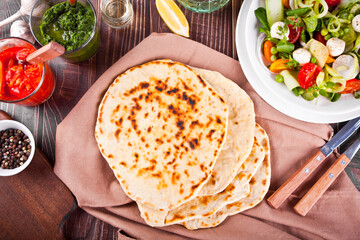 Homemade Indian naan flatbread with fresh salad and dips on the dinner table. Top view.