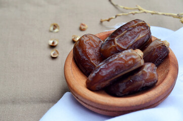 Dates (Phoenix dactylifera) on a wooden bowl on a white and brown cloth background. food for breaking the fast during Ramadan for Muslims. selective focus
