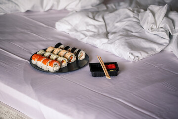 A plate with a sushi set stands on a white bedspread, rolls for a romantic dinner. Traditional japanese food