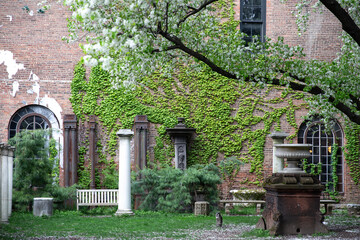 New York City - April 18 2021: Red brick building covered in ivy with ornamental columns and figures in Elizabeth Street Garden in Nolita, Manhattan.