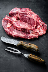 Raw meat Ribeye Steak with seasoning, with meat knife and fork, on black stone background